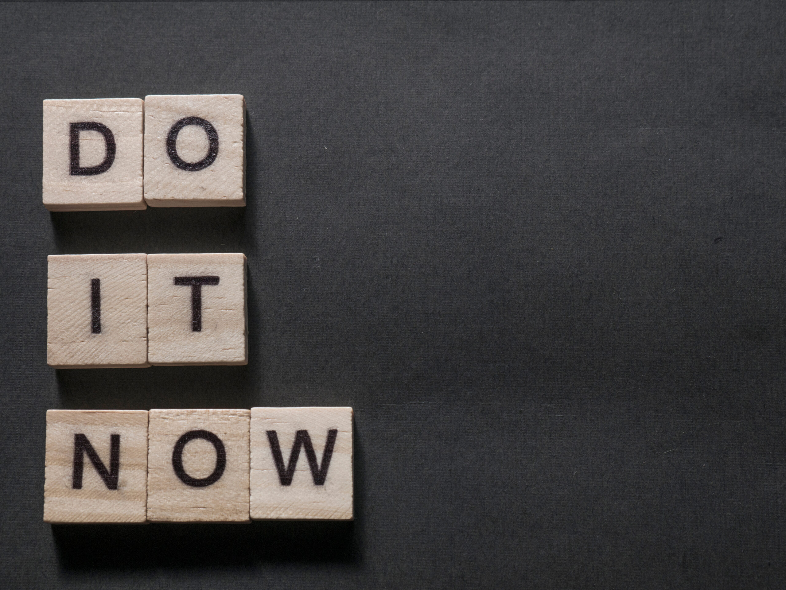 Wooden letter tiles spelling Do It Now on dark background representing motivational morse code bracelet inspiration