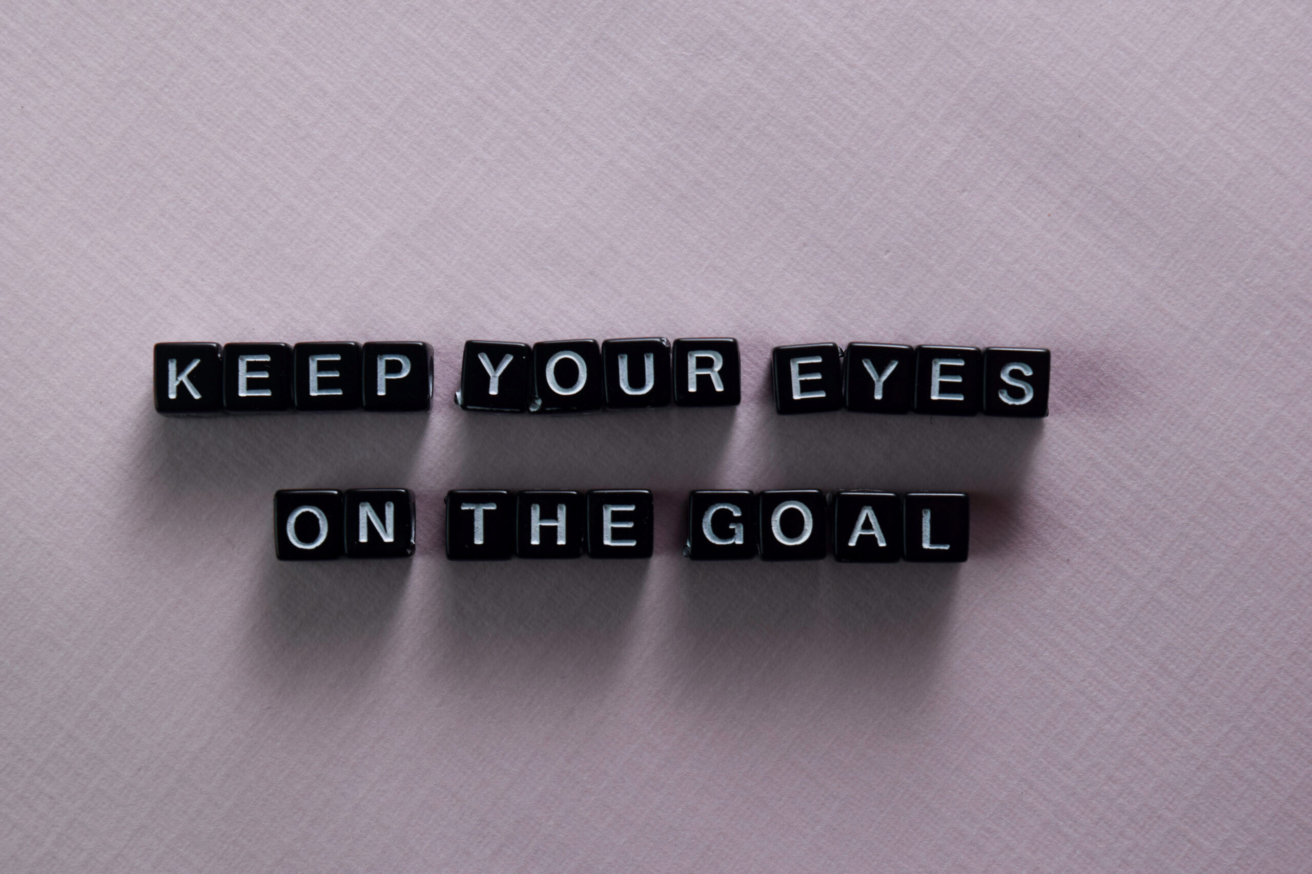 Black letter beads spelling Keep Your Eyes On The Goal on pink background representing hidden message morse code bracelet