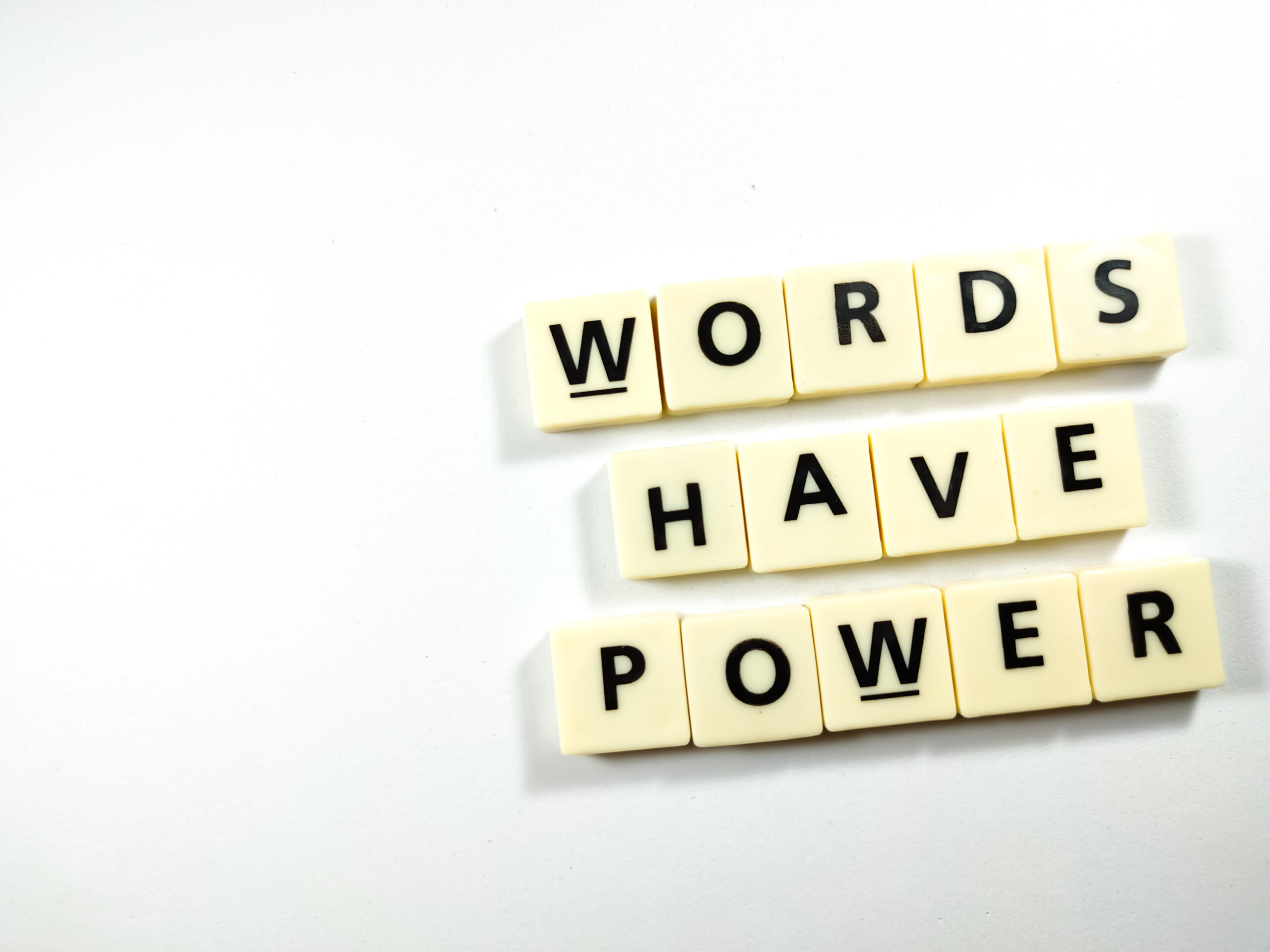 Cream colored letter tiles spelling Words Have Power on white background representing secret message morse code bracelet
